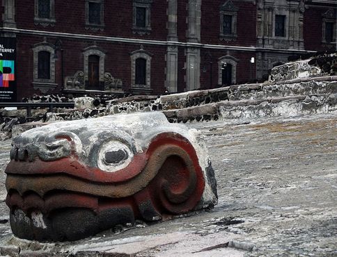 Раскрашенная каменная змеиная голова на фоне Площади Конституции