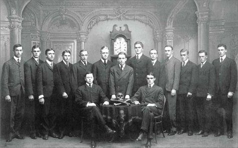 Архивная фотография 15 членов общества "Череп и кости" на фоне напольных часов