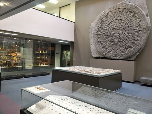 Копия ацтекского каменного календаря и монеты Древнего Рима на переднем плане