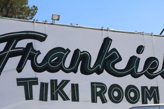 Вывеска Frankie's Tiki Room ночью светится розовым