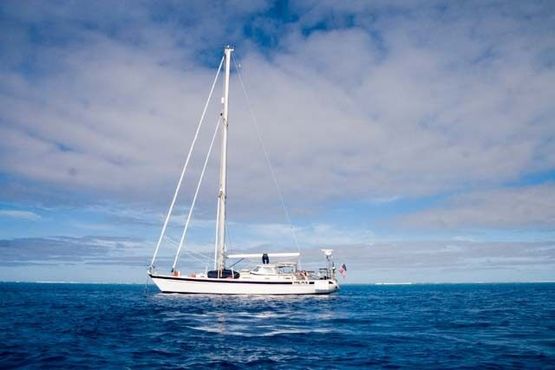 Яхта, поставленная на якорь у рифа Южная Минерва в Тихом океане. Риф виднеется на заднем плане